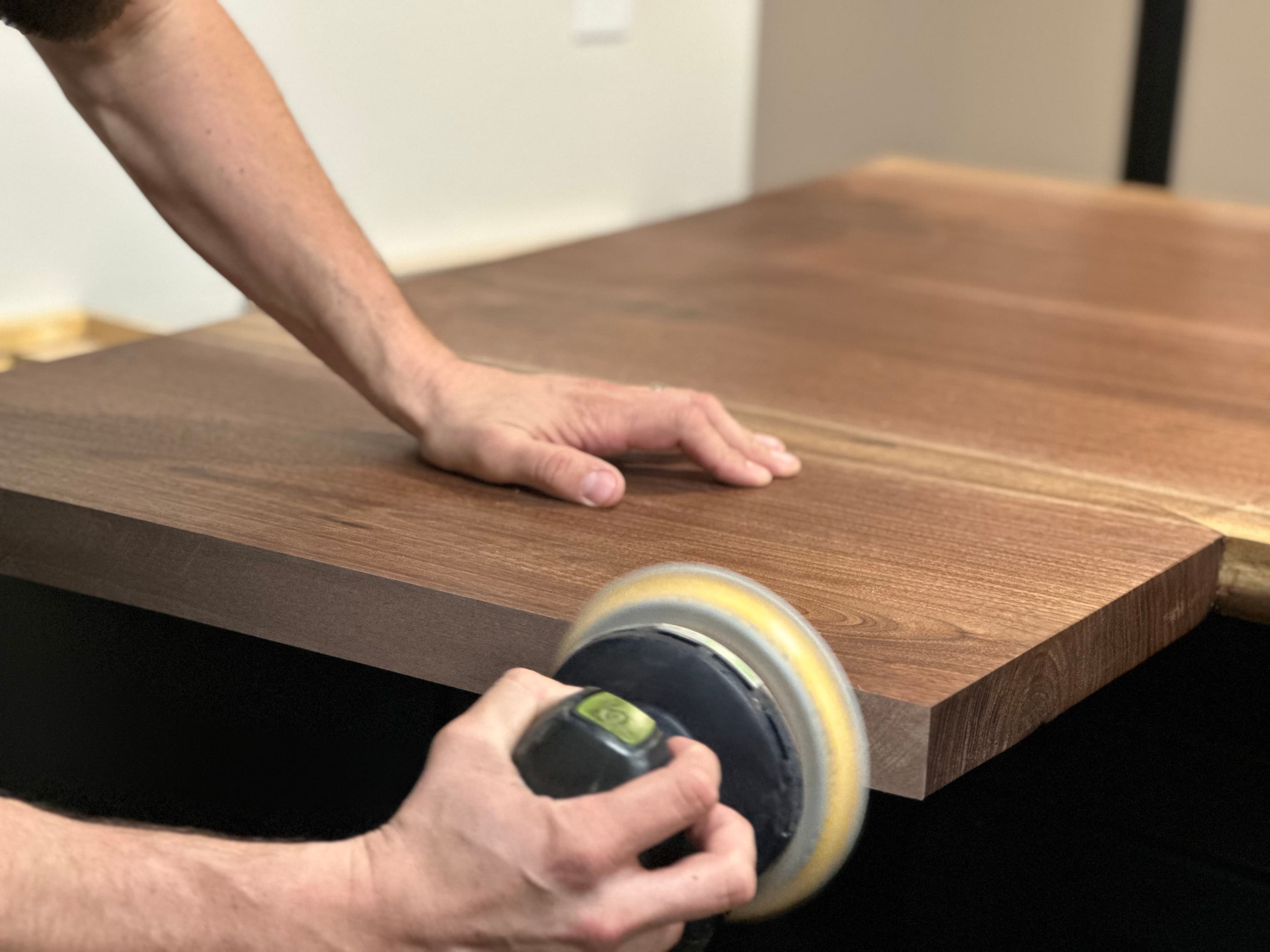The maker hand-sanding a black walnut top in the Lineage Craft Co. studio